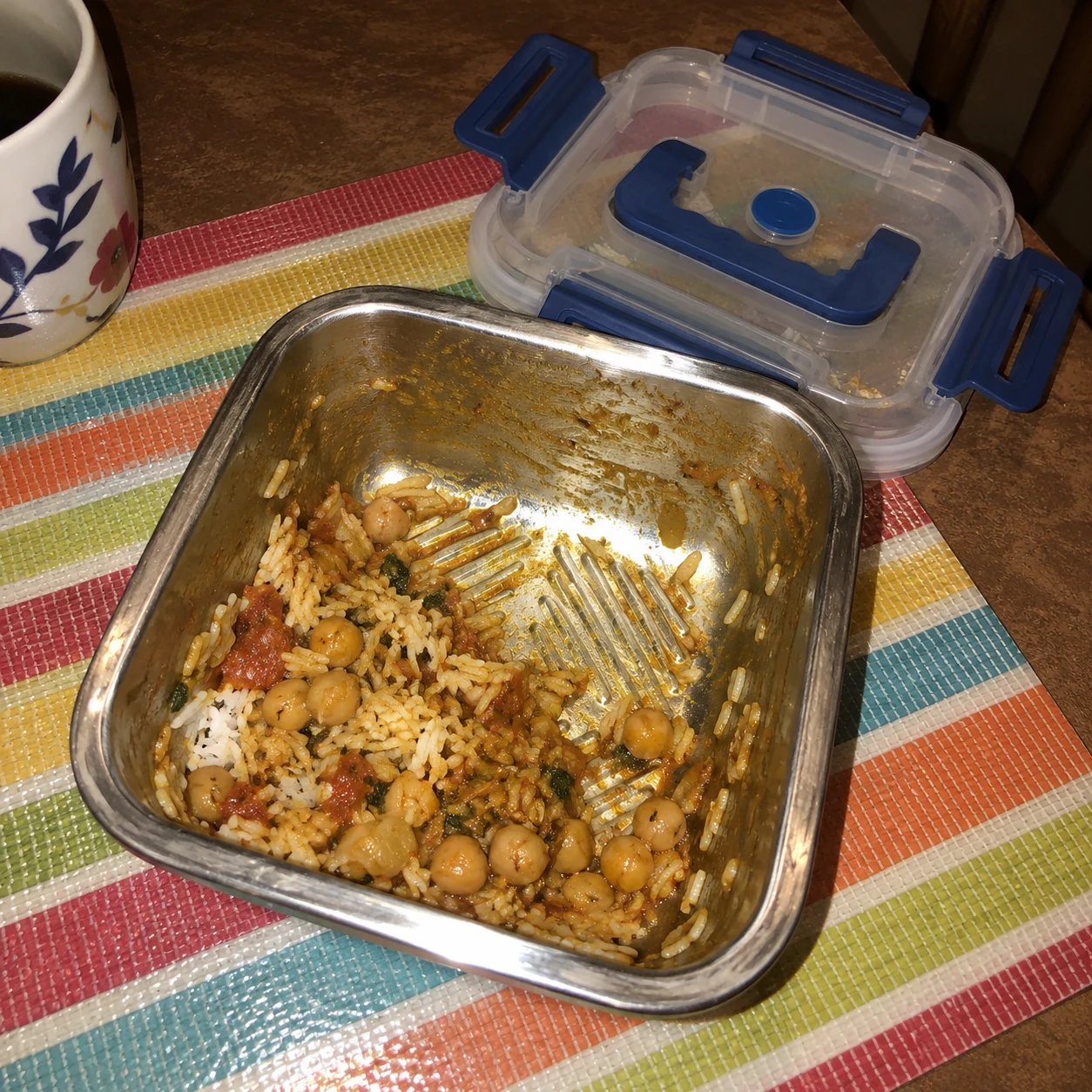 Leftover curry and rice in a steel container photographed with a phone flash at a dining table
